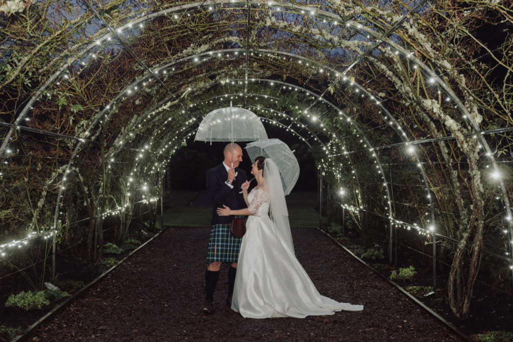 Bride and Groom with unbrellas under rose pergola at night